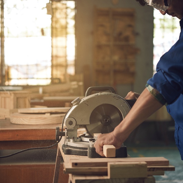 Hands of carpenter using circular saw to cut wooden piece